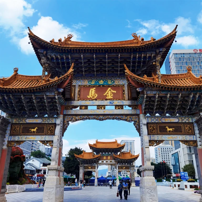 Kunming Jinma Biji Archway 昆明金馬碧雞坊矗立於廣場,藍天下的傳統建築展現飛簷翹角與精美彩繪。牌坊刻有「金馬」字樣,與後方現代城市建築交織。